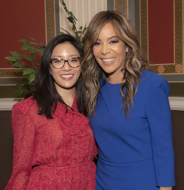 Zwei Frauen in Kleidern stehen strahlend nebeneinander, eine in Blau und eine in Rot mit Brille, bei der 2019 Women in Film Pre-Oscar-Luncheon.
