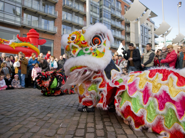 Eine Löwen-Tanzvorführung während eines chinesischen Neujahrsfestes in Amsterdam mit einer Zuschauermenge und Gebäuden im Hintergrund.
