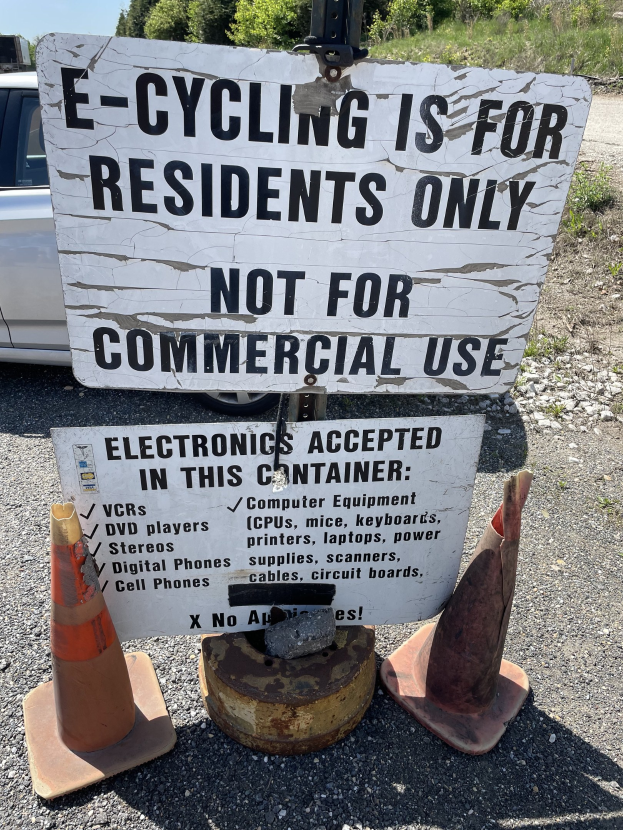 Schilder mit der Aufschrift "e-Bike-Fahren nur für Anwohner" neben einer Straße mit Absperrbaken, einem Fahrzeug, Bäumen und einem klaren blauen Himmel im Hintergrund.