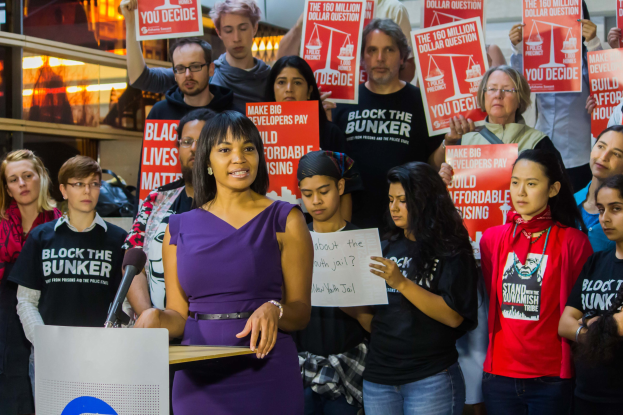 Eine Black Lives Matter-Aktivistin spricht an einem Rednerpult mit Mikrofon zu einer Menge mit Schildern.