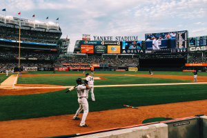 Baseballspiel im Yankee Stadium mit Spielern und Zuschauern, umgeben von Stadionmerkmalen unter einem bewölkten Himmel.