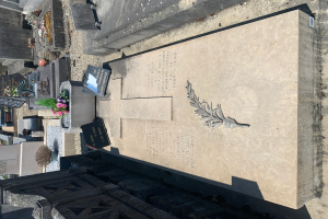 Ein Friedhof mit einem Grab in der Mitte, geschmückt mit einem Kranz, umgeben von Blumentöpfen mit Pflanzen und Blumen und einem Gebäude im Hintergrund.