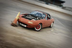 Eine Person fährt mit einem roten Auto auf einer Rennstrecke mit hoher Geschwindigkeit und einem Verkehrskegel vorne.