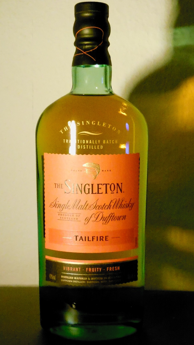 Eine tiefe bernsteinfarbene Flasche Singleton of Dufftown Tailfire Single Malt Scotch Whisky mit einem schwarzen Etikett, das eine Schrift in fetter schwarzer Schrift und ein Wappen mit einem Löwen und einer Burg zeigt.