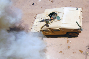Panzerfahrzeug fährt auf einer Schotterstraße mit Rauchentwicklung und einer Person im Inneren.