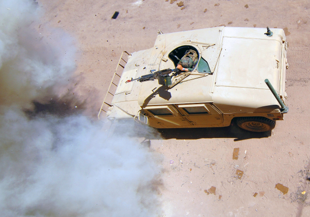 Panzerfahrzeug fährt auf einer Schotterstraße mit Rauchentwicklung und einer Person im Inneren.