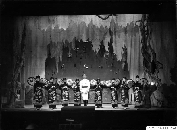 Schwarzes und weißes Foto von Darstellern in traditionellen japanischen Kimonos auf einer Bühne mit einem gemalten Hintergrund, beschriftet mit 'Kimono-Show in Tokyo, Japan.'