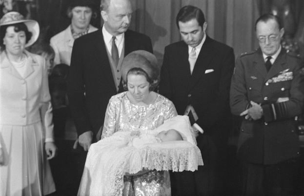 Königin Elizabeth II. wiegt ihren neugeborenen Sohn Prinz Philip, während Prinz Philip, Herzog von Edinburgh, neben ihr in einem Anzug und Schlips steht, mit Vorhängen im Hintergrund.
