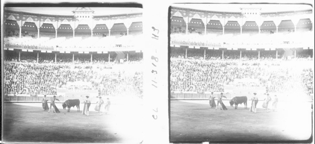 Schwarzes und weißes Foto von einer Stierkampfveranstaltung in einem Stadion mit Zuschauern auf den Rängen und einer Gruppe von Menschen und Tieren im Vordergrund.
