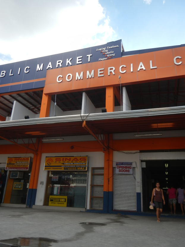 Ein öffentlicher Markt mit einem Geschäftszentrum, vor dem Menschen gehen, mit Text auf dem Gebäude und einem sichtbaren Himmel oben.