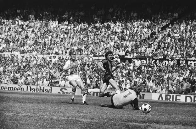 Schwarzes Foto von Männern beim Fußballspielen auf einem Feld mit Zuschauern im Hintergrund und einer Bundesliga 1978-79 Ajax 1-1 Hannover 96-Banner.