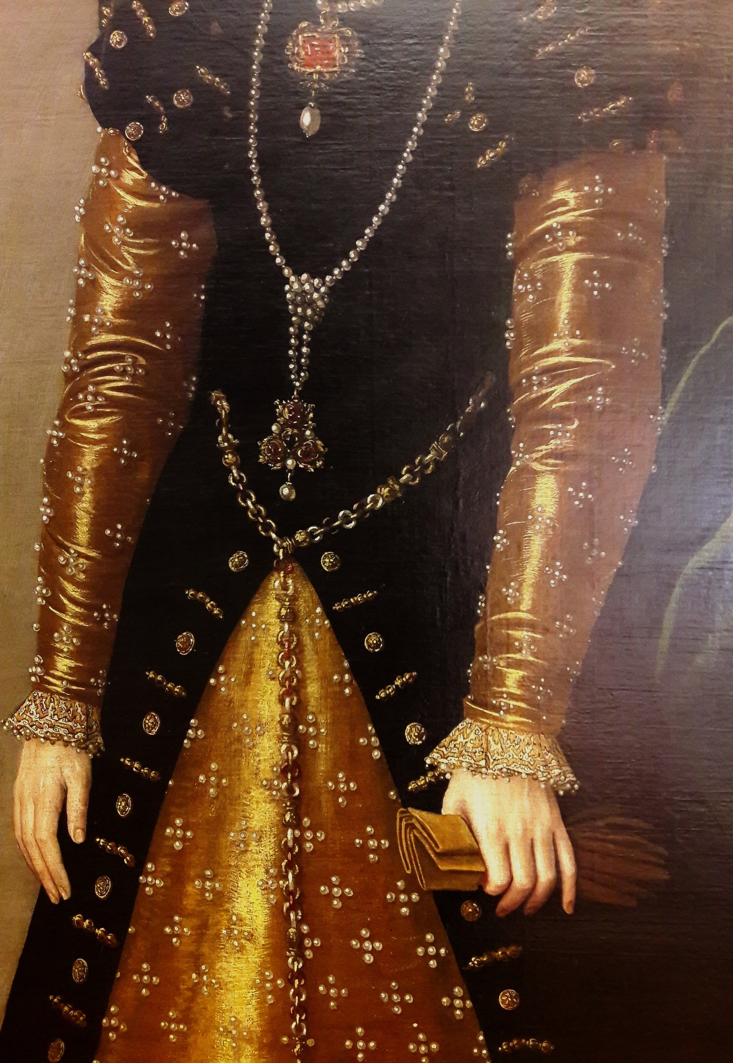 Bild einer Frau in goldnem Kleid mit hohem Ausschnitt und langen Ärmeln, die eine Tasche hält und deren Haar zu einem Knoten gebunden ist.