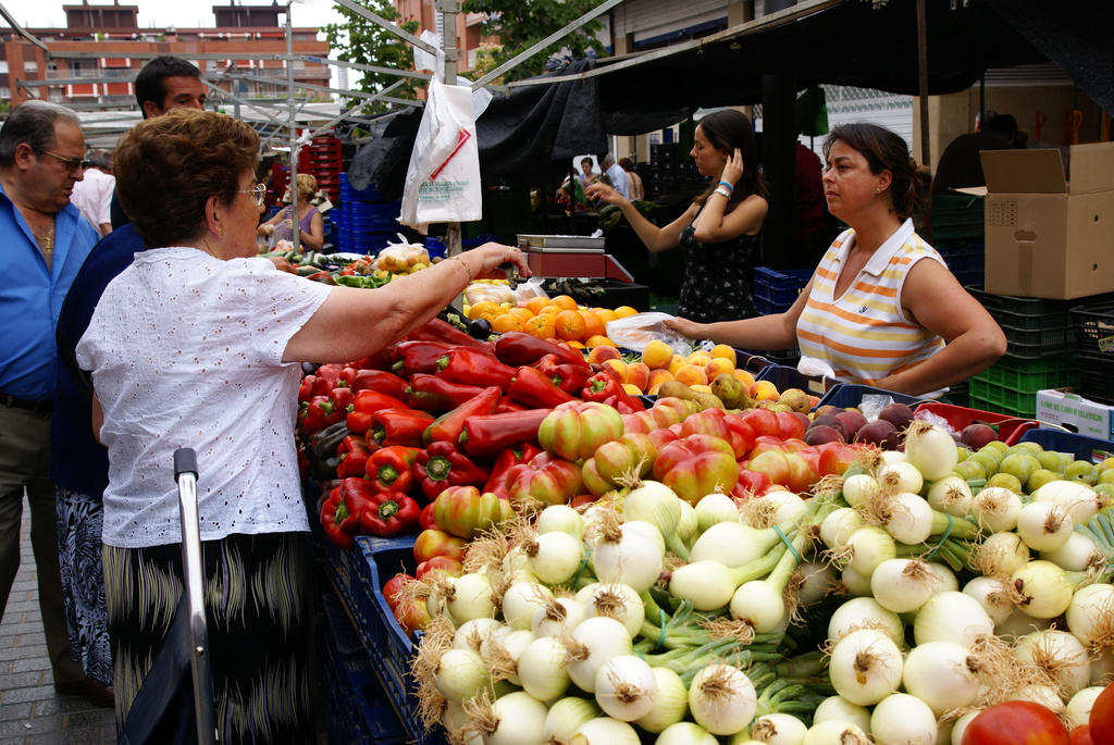 Eine Gruppe von Menschen steht draußen in der Nähe von Gebäuden und Bäumen, mit Gemüse in Plastikbehältern und einer Kartonschachtel in der Nähe.