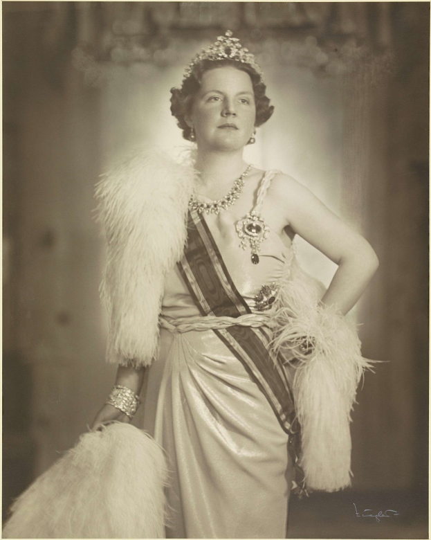 Schwarz-weiß-Foto von Queen Elizabeth II in einem Kleid und einer Krone mit einem unscharfen Hintergrund und Text unten.