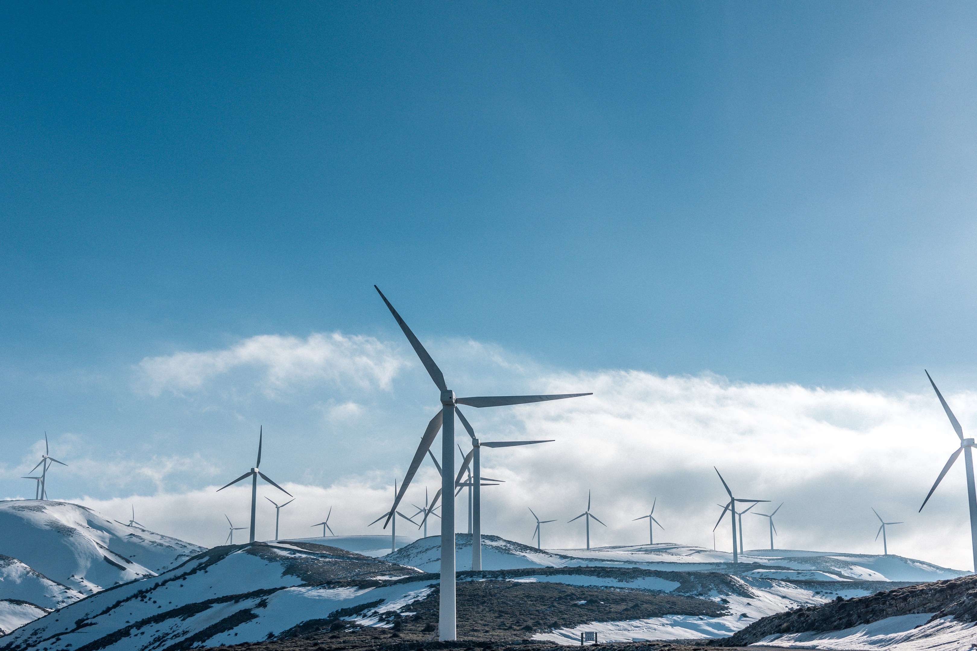 Eine Gruppe von Windkraftanlagen in einem verschneiten Feld mit schneebedeckten Hügeln und Wolken im Hintergrund, Teil eines Erneuerungsenergieprojekts.