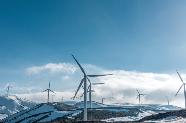 Eine Gruppe von Windkraftanlagen in einem verschneiten Feld mit schneebedeckten Hügeln und Wolken im Hintergrund, Teil eines Erneuerungsenergieprojekts.