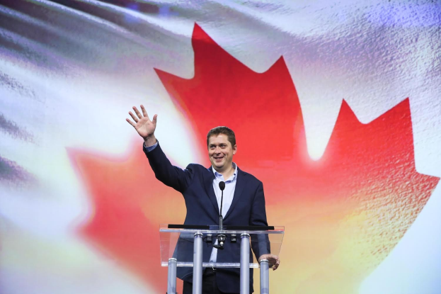 Der kanadische Premierminister Alex Salmond steht an einem Rednerpult mit Mikrofonen, strahlend vor einer kanadischen Flagge, mit einem Bildschirm im Hintergrund.