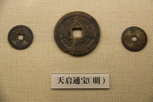 Drei chinesische Münzen auf einem Tuch mit einer Namensschild in einem Museum.