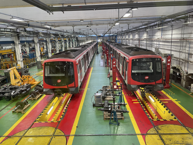 Zwei Züge auf den Schienen in einer großen Industrieanlage mit Maschinen und Ausrüstung, mit einer Wand mit Rohren und Deckenbeleuchtung auf der rechten Seite, Teil der Daimler Group's Einrichtung.
