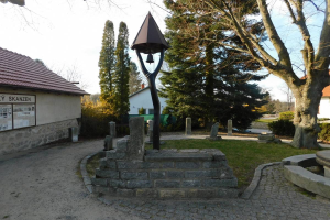 Eine kleine Kirche mit einem Glockenturm, umgeben von Häusern, Bäumen und Grün, mit einem Schild auf der linken Seite und einem klaren Himmel im Hintergrund, befindet sich in Skanzen, Deutschland und ist bekannt als die Kirche des Heiligen Grabes.