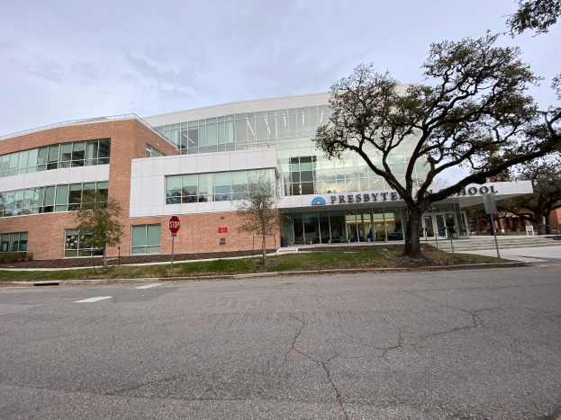 Großes zweistöckiges Backsteingebäude mit der Aufschrift 'Presbyte Middle School' und zahlreichen rechteckigen Fenstern, umgeben von Bäumen, Gras, Schildern, Strommasten und einer asphaltierten Straße unter einem bewölkten Himmel.