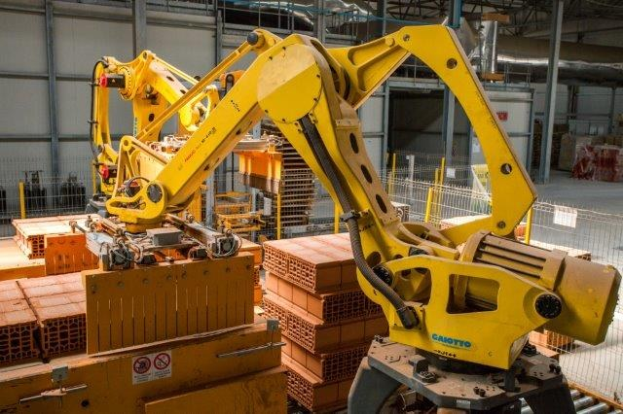 Großes Industriegebäude mit gestapelten Kisten, Kränen, Zaun, Strommasten und einer fernen Mauer.