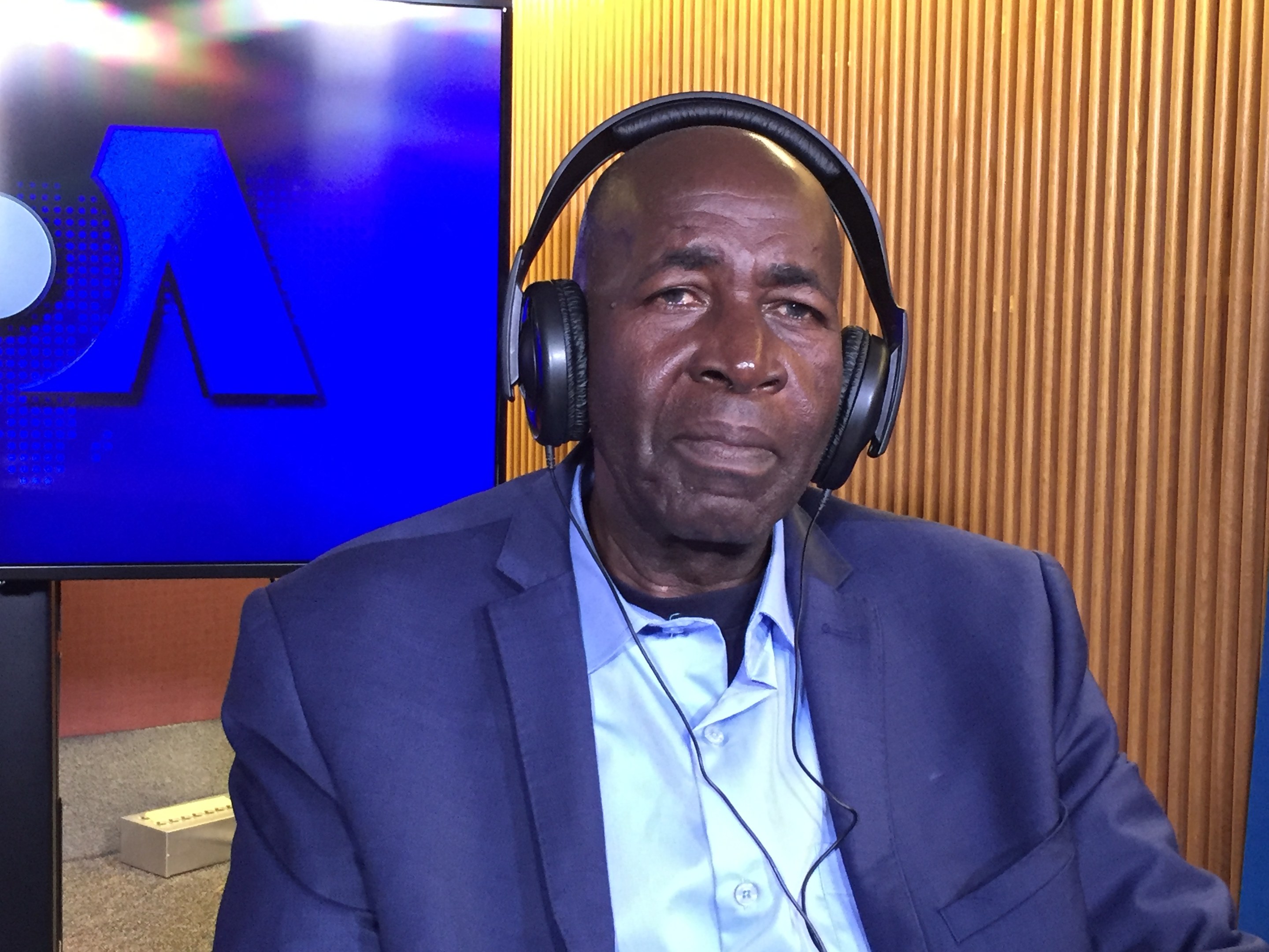 Ein Mann in Anzug und Kopfhörern sitzt vor einem Fernseher mit einer hölzernen Wand im Hintergrund und scheint während einer Diskussion über das Internetverbot der nigerianischen Regierung zu sprechen.