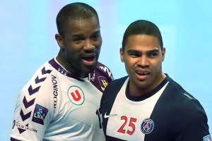 Zwei Männer in weißen und blauen T-Shirts auf einem Fußballfeld mit einem hellblauen Hintergrund, die einen Sieg feiern.