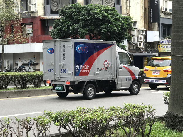 Ambulanz am Straßenrand neben einem Baum geparkt mit Fahrzeugen, Gebäuden und anderen Objekten im Hintergrund.