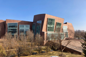 Großes Gebäude mit zahlreichen Fenstern, umgeben von Bäumen, Bänken, Gras und einem Lichtmast, vor anderen Gebäuden und einem klaren blauen Himmel, als der neue Campus der University of Illinois at Chicago identifiziert.