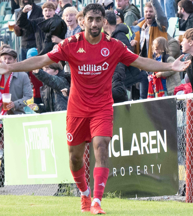 Ein Fußballspieler in roter Uniform rennt mit ausgestreckten Armen auf einem Feld, umgeben von Zuschauern, mit einem Banner im Hintergrund, auf dem "Middlesbrough FC gegen Swansea City - Sky Bet Championship" steht.