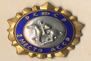 Gold- und blaues Kreisabzeichen mit einem Pferd und Reiter, mit Text rundherum, in der Mitte des Bildes.