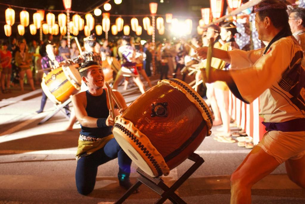 Männer, die auf einem Festival Trommeln spielen, mit Lichtern, die darüber hängen.