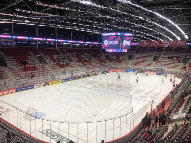 Hockey-Spiel in einer großen Arena zwischen den St. Louis Blues und Detroit Red Wings, mit Zuschauern auf den Sitzen und Stehplätzen in der Nähe der Eisfläche, umgeben von einem Zaun, einem Bildschirm, Metallrahmen und Deckenleuchten.