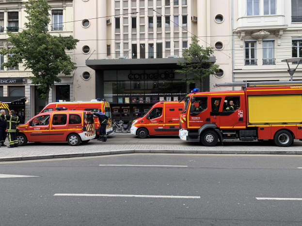 Eine Gruppe von Feuerwehrautos auf einer Pariser Straße geparkt mit Menschen in der Nähe, vor Häusern, Bäumen und einem Fahrrad.