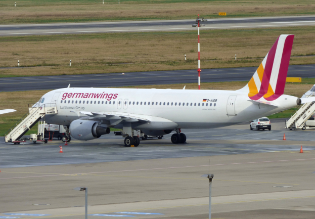 Germanwings Airbus A320-200 am Frankfurter Flughafen geparkt mit Bodenfahrzeugen, Verkehrskegeln, Versorgungsmasten und grüner Fläche im Hintergrund.