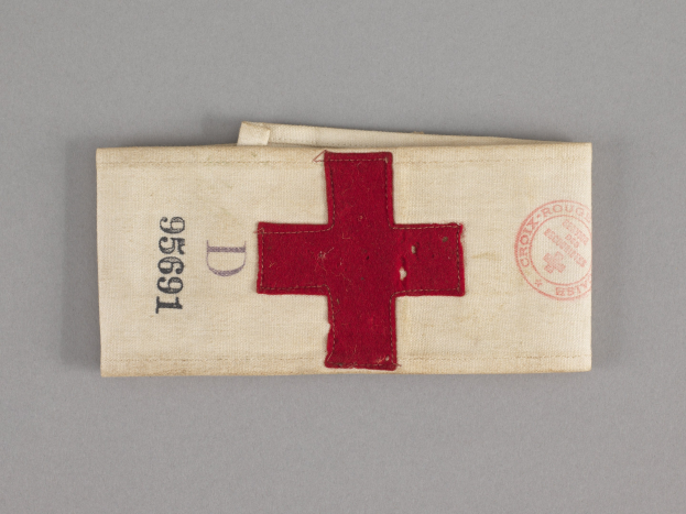 Ein rotes Kreuzes-Notfallkit in einem Stoffbeutel mit Text und einem Stempel, das auf einer Oberfläche liegt.