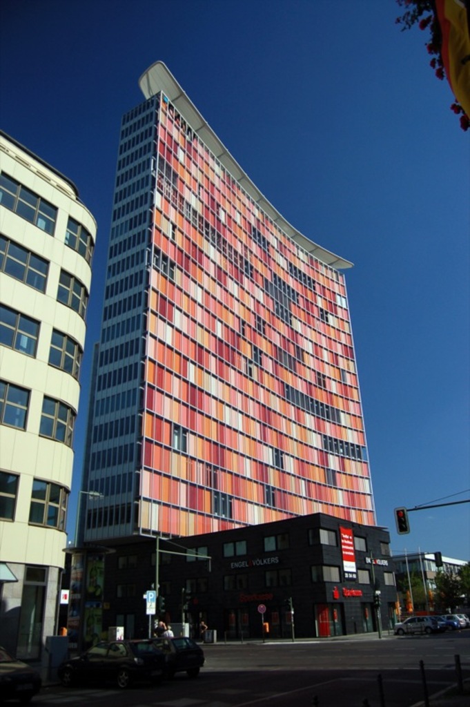 Hohe Gebäude mit parkenden Autos in einer Parkfläche und ein Verkehrsampelmast auf der rechten unteren Seite.